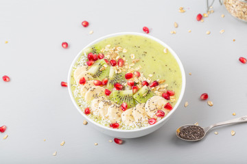 Healthy breakfast detox green smoothie with banana, kiwi, spinach, chia and pomegranate seed in a Bowl. Vegan food.