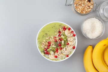 Healthy breakfast detox green smoothie with banana, kiwi, spinach, chia and pomegranate seed in a Bowl. Vegan food. Top view.