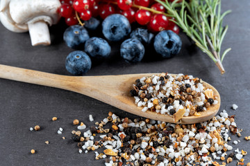 Mit Pfeffer gefüllter Holzlöffel auf einer Schiefertafel und im Hintergrund diverse Zutaten