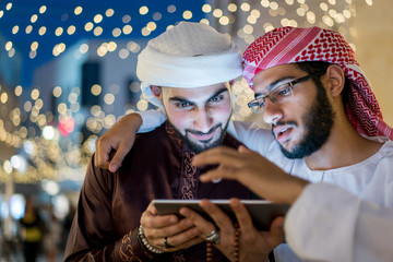 Two Arab men with tablet in city at night