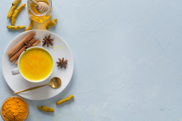 Obraz na płótnie Canvas Golden turmeric milk with honey and ingredients on blue. Space for text or recipe. Healthy drink for immunity. Top view. Natural food