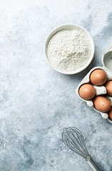 Raw eggs and wheat flour in a bowl on gray stone background. Flat lay. Copy space. Homemade food concept