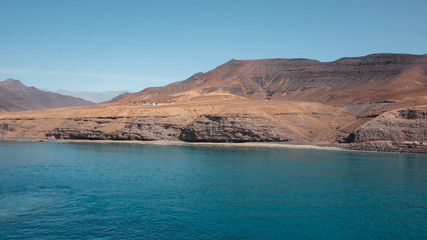 Fototapeta na wymiar Approaching Fuerteventura island at its most southern point, at Morro Jable with the display of the solitary cliffs and arid mountains behind, part of the Parque Natural Jandia, Canary Islands, Spain