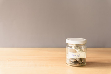 Coin in a glass jar on wooden desk, Saving money for travel concept