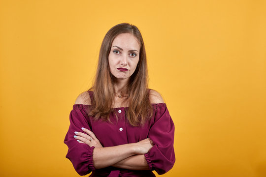 Ginger girl in burgundy bluse with bow over isolated orange background looks angry and folding her armes