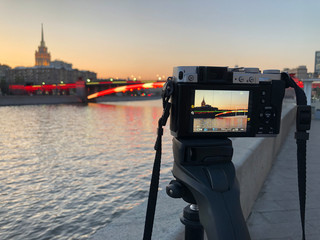 Digital camera stands on the tripod with cityscape on the live view and the same blurred cityscape at the background