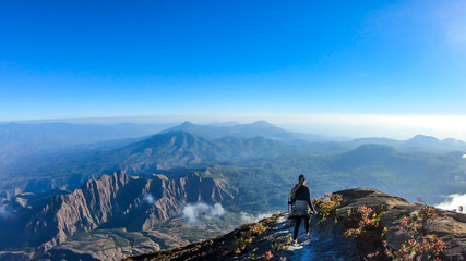 A young woman walking down the volcano Inierie in Bajawa, Flores, Indonesia. She supports herself on a wooden stick while enjoying the beautiful view on volcanic island. Lots of fluffy clouds around © Chris