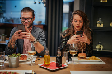 Bored couple sitting in restaurant for dinner and using smart phones. - Powered by Adobe