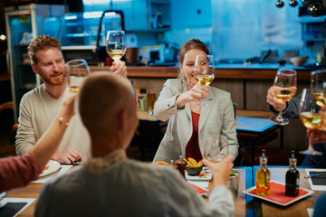 Group of best friends sitting in restaurant for dinner and making a toast with wine.