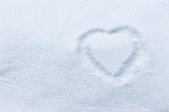 Heart in the snow, hands drawing on a clean empty snow surface, winter cold. Concept of love, love message winter outdoors