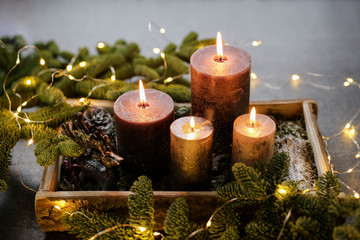 Christmas candles, dark and silver in a wooden stand, with moss, tree branches, cones on a dark background.