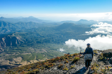 Obraz premium Young woman walking down the steep road on a gravelled volcano Inierie's side in Bajawa, Flores, Indonesia. She supports herself on a wooden stick while enjoying the beautiful view on volcanic island