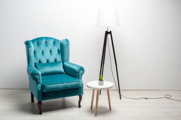 elegant velour blue armchair with pillow near coffee table and floor lamp