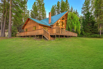 Luxury summer mountain cabin home with large green lawn and pine trees.