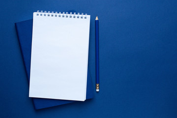 White, blue office notebook and pencil on a classic blue background. Trendy color 2020