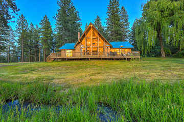 Luxury summer mountain cabin home with large green lawn and pine trees.