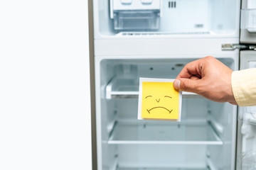 cropped view of man holding sad smiley near empty open fridge isolated on white
