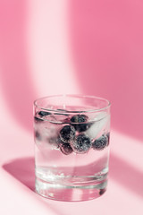 fresh lemonade with ice and blueberries in sunlight on pink background