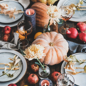 Fall Table Setting For Thanksgiving Day Or Family Gathering Dinner. Plates, Silverware, Floral And Fruits Decoration, Candles And Pumpkins Over Rustic Wooden Table Background, Square Crop