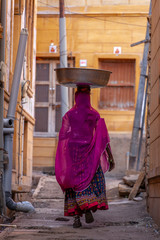 A woman carrying on her head in a street of Jaisalmer in Rajasthan, India