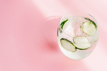 fresh lemonade with ice and cucumber slices on pink background with sunlight