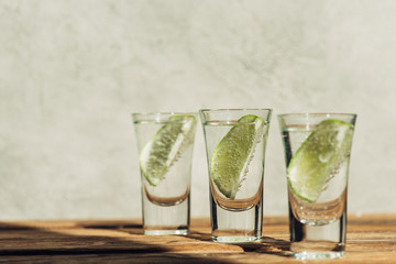 selective focus of fresh tequila with lime on wooden surface in sunlight