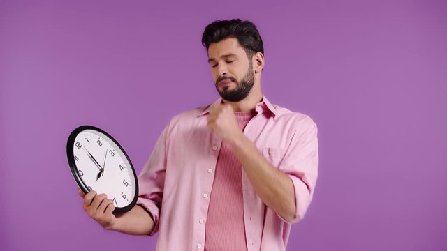 shocked man looking at clock isolated on purple