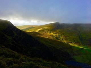 The setting sun shines through the hills and illuminates the valley in Ireland