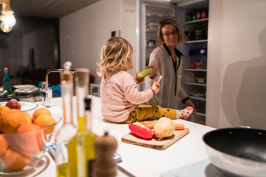 Little girl sitting in the kitchen with her mother giving her a banana