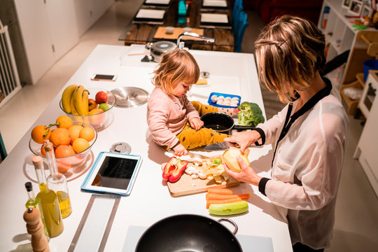 Mother preparing food in the kitchen with a little girl sitting next to her