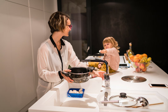 Mother preparing dinner in the kitchen with a little girl sitting next to her, showing her an egg
