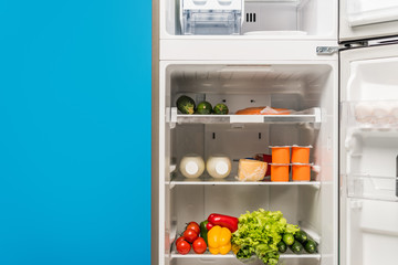 open fridge full of fresh food on shelves isolated on blue