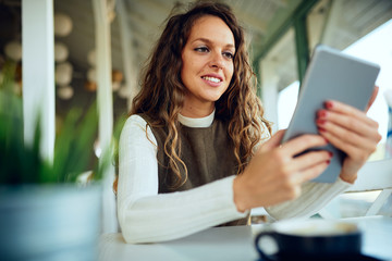 Attractive young curly brunette looking at her tablet and smiling	