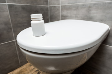 container with pills on ceramic clean toilet bowl in modern restroom with grey tile