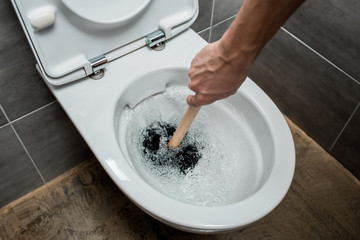 cropped view of plumber using plunger in toilet bowl during flushing in modern restroom with grey...