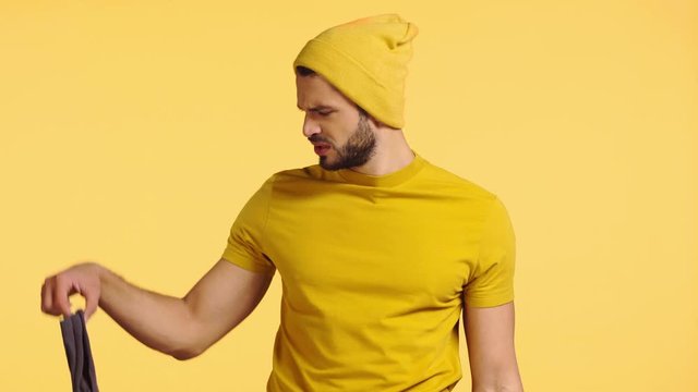 dissatisfied man smelling stinky socks isolated on yellow