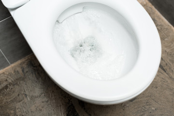 clean white toilet bowl with flushing in modern restroom with grey tile