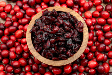 Natural source of minerals, vitamins and essential nutrients, organic berries and diet rich in antioxidants conceptual idea with wooden bowl of dried cranberries surrounded by raw cranberry heap