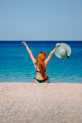 Happy woman enthusiastically raises her hands up sitting on beach