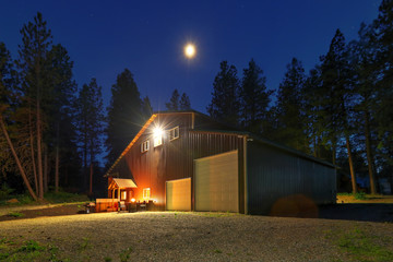 Large metal barn at night with fire at round table and outdoor furniture. - Powered by Adobe