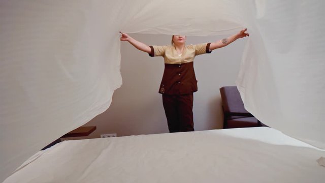 Chambermaid makes bed in hotel bedroom. Slow motion