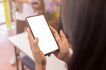 Asian woman is using a smartphone in a coffee shop with white sceen and clipping path. Mobile phones with white screens on the hands of women in convenience stores.