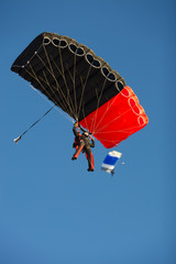 Figure skydiver under a bright black and red canopy of a parachute before landing on a background of blue sky close-up.