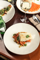 Tasty healthy fish fillet with baby carrots and glass of white wine wooden on table at restaurant
