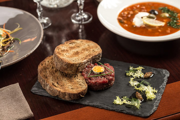 Steak Tartare with bread toasts served on stone plate on wooden table at restaurant