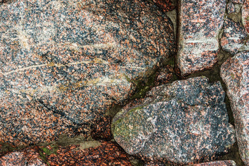 background of a fragment of a stone wall of natural granite stones interspersed with different...