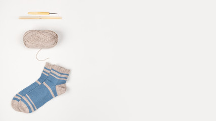 Wooden knitting needles, bamboo hook, ball of beige yarn and blue-grey socks from wool. Copy space. Crochet work. Flat lay. Needlework and leisure concept. Female hobby. Template for your design.