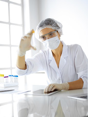 Professional female scientist in protective eyeglasses researching tube with reagents in laboratory. Concepts of medicine and research