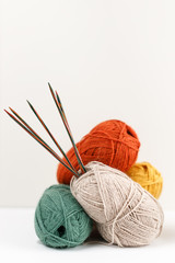 Red, green, yellow and beige clews of yarn of pastel colors. Multicolored wooden knitting needles stuck in the ball. Template for your design. Female hobby. Needlework and leisure concept. Copy space.