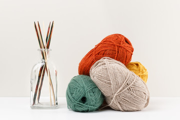 Multicolored bamboo wooden knitting needles in glass jar and red, green, yellow and beige pastel colored clews of yarn. Selective focus. Needlework and leisure concept. Template for your design.